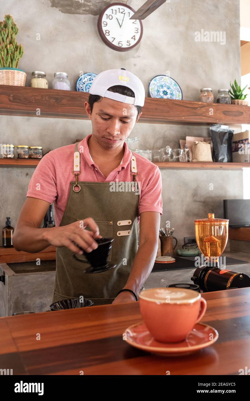 Barista Asian Smiling on Duty service proposant du café Cappuccino avec Un professionnel Smile Bright Morning Light Banque D'Images