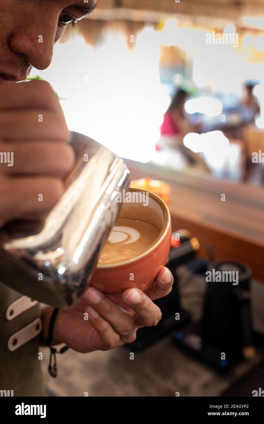 Barista Asian Smiling on Duty service proposant du café Cappuccino avec Un professionnel Smile Bright Morning Light Banque D'Images