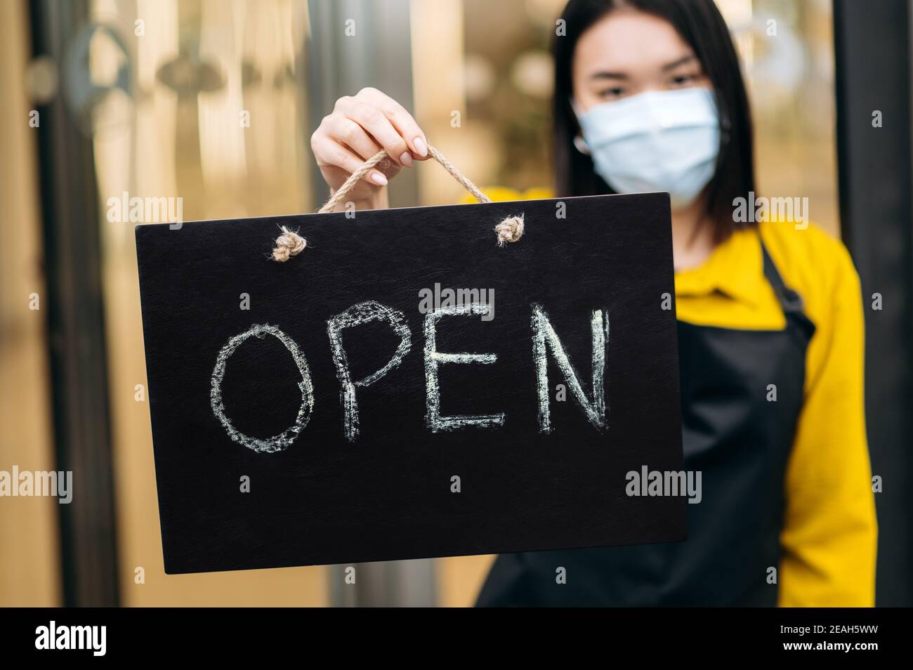 Panneau ouvert au premier plan. Une servante défoquée dans un masque médical protecteur sur son visage, tient l'affiche OUVERTE à l'entrée d'un restaurant ou d'un café. Concept de petite entreprise Banque D'Images