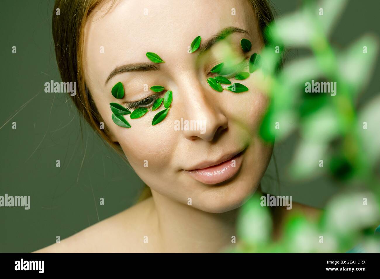 Portrait de jeune femme avec maquillage naturel flou avec la branche de buis défocused. Les feuilles vertes se patch sur le visage. Concept de médecine à base de plantes. Banque D'Images
