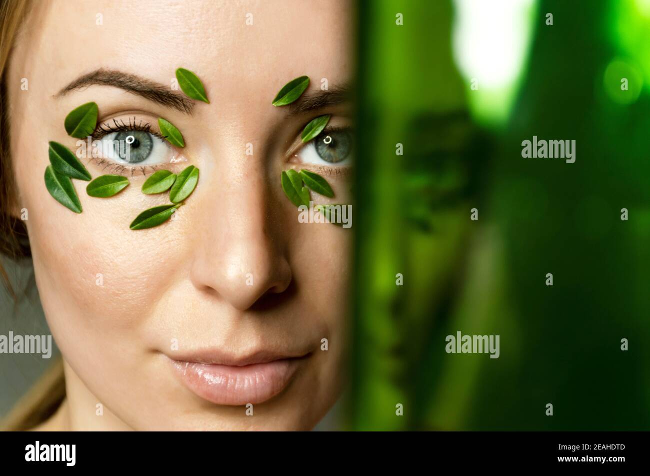 Gros plan des yeux de la jeune femme avec des feuilles de buis patch avec un espace de copie vert flou. Bannière de modèle de spa et de bien-être pour le design. Banque D'Images