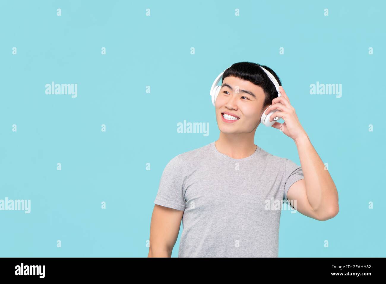 Un jeune homme asiatique heureux portant un casque sans fil pour écouter de la musique et souriant sur fond bleu clair Banque D'Images
