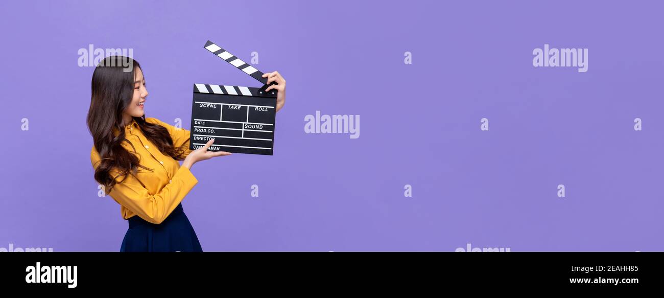 Jeune belle fille asiatique tenant un film clapperboard isolé sur violet arrière-plan de bannière avec espace de copie Banque D'Images