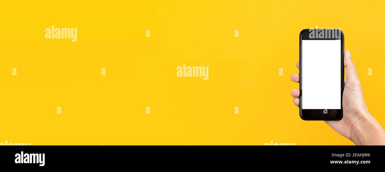 Main tenant le téléphone mobile sur fond de bannière jaune coloré avec écrans vides pour le montage de vos textes ou images Banque D'Images