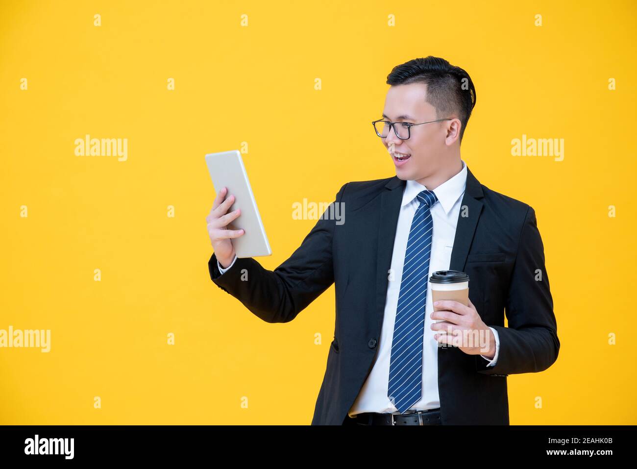 Homme d'affaires asiatique concentré qui cherche une tablette tout en buvant du café isolé sur fond jaune Banque D'Images