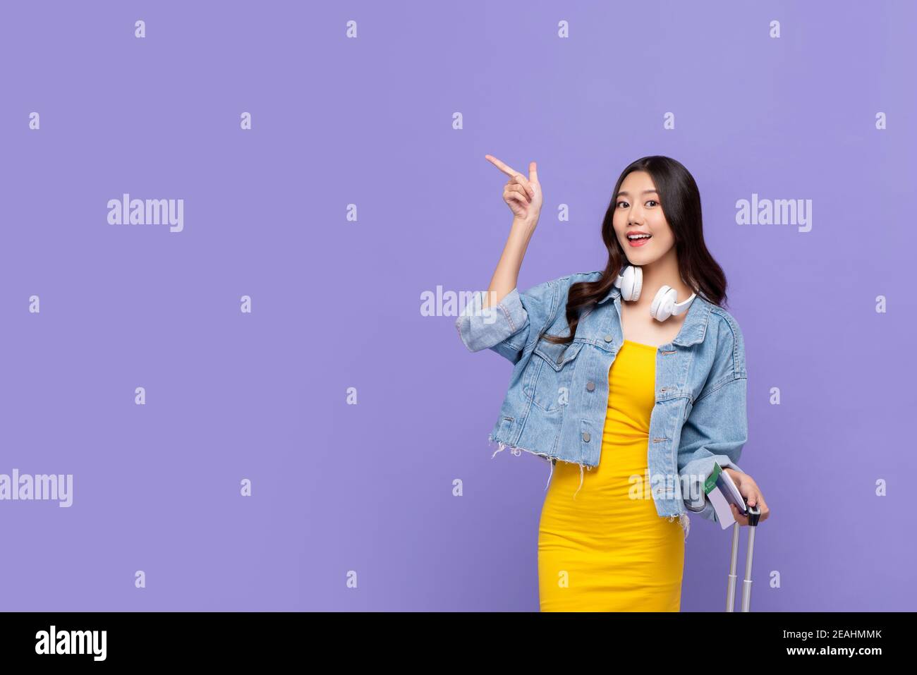 Souriante, jolie femme asiatique touristique prête à partir en voyage en pointant la main pour copier l'espace de côté de l'arrière-plan violet isolé Banque D'Images