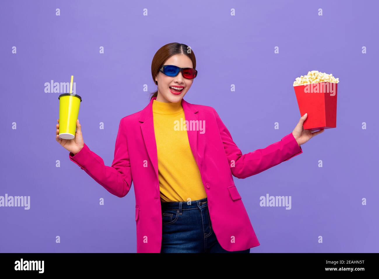 Jeune femme asiatique portant des lunettes 3D pour regarder un film avec buvez et popcorn dans les mains sur fond violet Banque D'Images