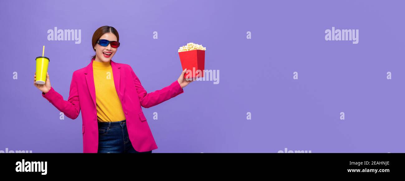 Jeune femme asiatique portant des lunettes 3D pour regarder un film avec buvez et popcorn en mains sur fond de bannière mauve avec copier l'espace Banque D'Images