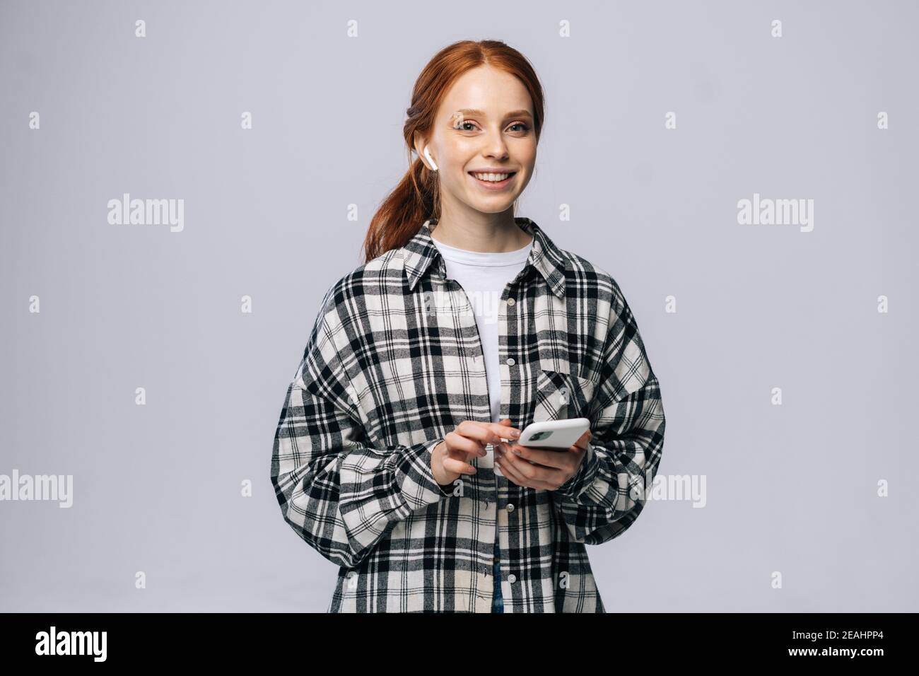 Magnifique jeune femme souriante, vêtue d'un casque sans fil, qui écoute de la musique depuis un smartphone. Banque D'Images