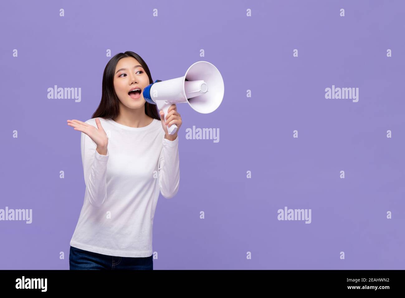 Belle femme asiatique annonçant sur le magaphone isolé sur fond violet avec espace de copie Banque D'Images