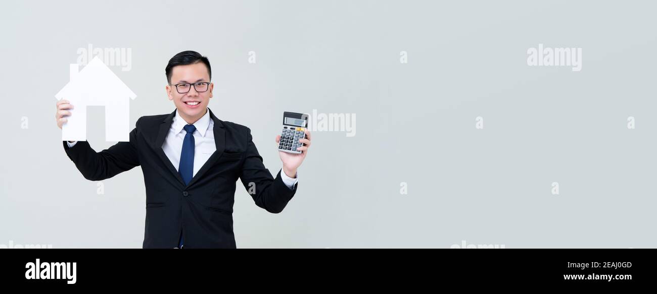 Agent homme asiatique montrant le modèle de maison avec la calculatrice sur gris arrière-plan de bannière avec espace de copie pour le financement immobilier et concept d'investissement Banque D'Images