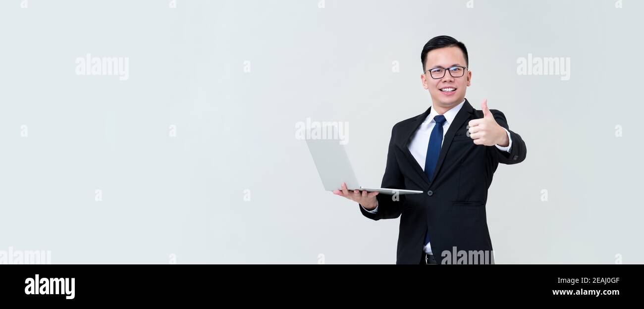 Un jeune homme d'affaires asiatique satisfait de ses activités en ligne ordinateur portable et de donner des pouces isolés sur fond de bannière grise avec espace de copie Banque D'Images