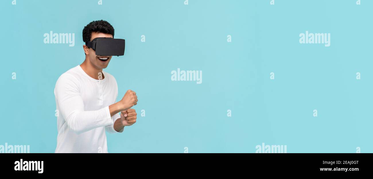 Un homme asiatique enthousiaste qui bouge tout en regardant une vidéo de simulation 3D Des lunettes de réalité virtuelle ou VR sur une bannière bleu clair arrière-plan avec espace de copie Banque D'Images