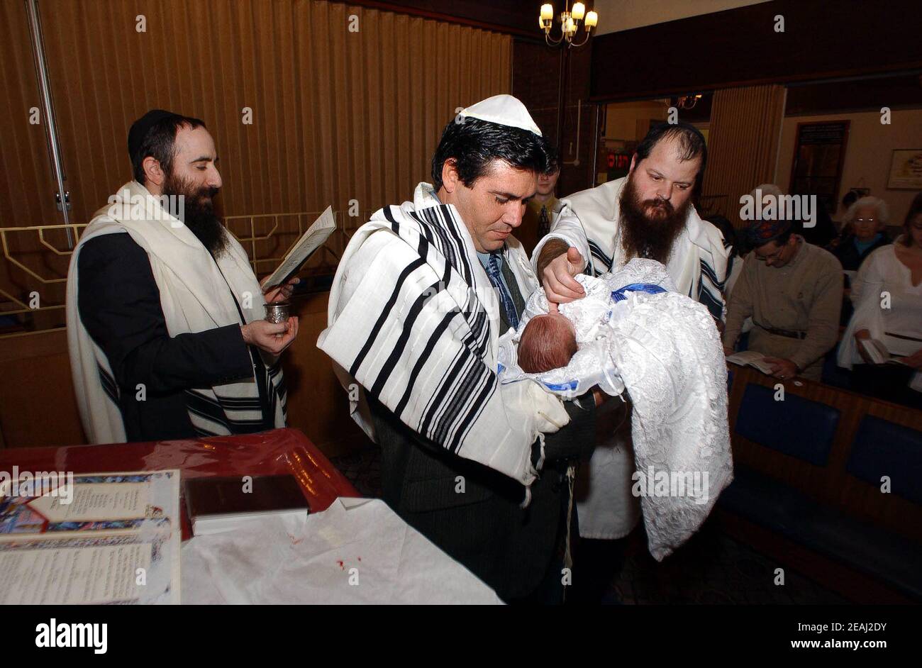 Une cérémonie de Brit Mila a lieu sur la bimah de la synagogue dans le Solihull, West Midlands, comme le Mohel donne les bénédictions traditionnelles comme il commence la circoncision surveillée par le rabbin et les membres de la famille. Banque D'Images