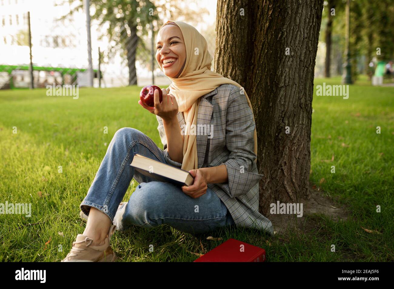 Une fille arabe dans le hijab tient une pomme et un manuel Banque D'Images