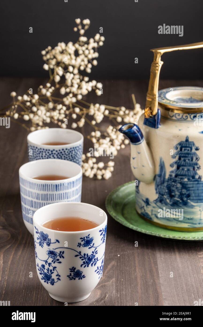 Vue de trois tasses bleues avec thé, fleurs blanches et théière en porcelaine, mise au point sélective, sur une table en bois, verticale Banque D'Images