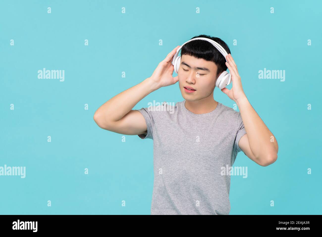 Homme asiatique en t-shirt gris décontracté avec casque à l'écoute musique émotionnelle avec les yeux isolés sur fond bleu clair Banque D'Images