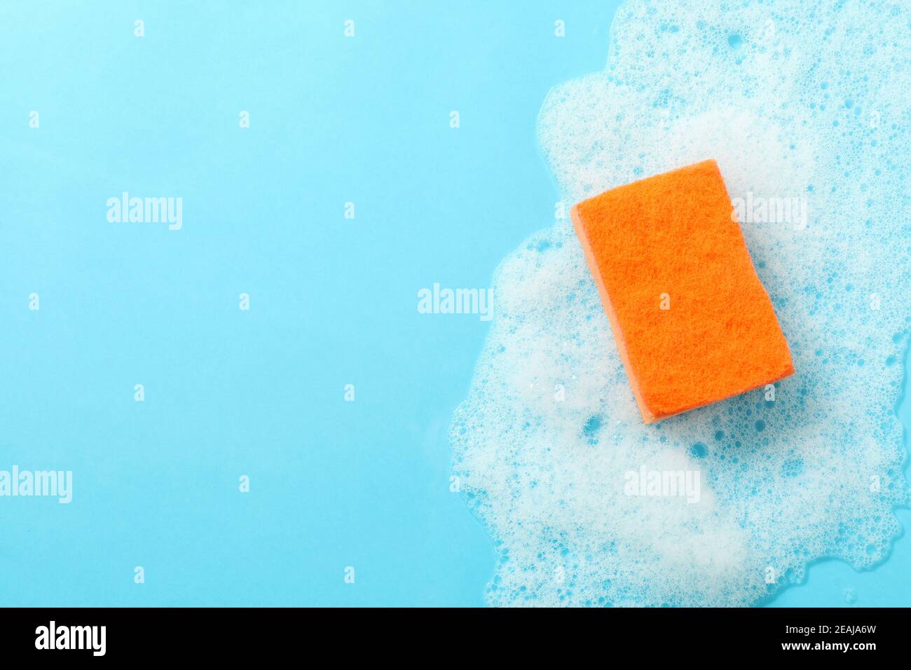 Éponge orange et mousse sur fond bleu Banque D'Images