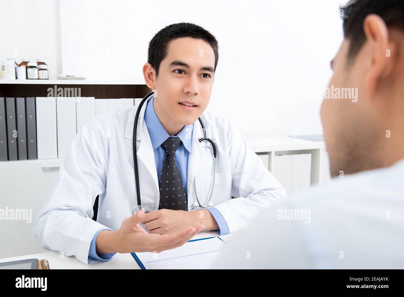 Jeune beau médecin asiatique parlant avec un patient masculin à l'hôpital Banque D'Images