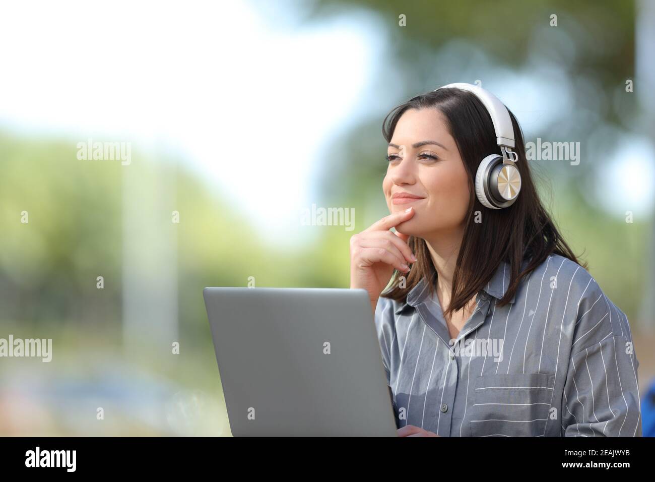Une femme avec un ordinateur portable et un casque pense à regarder de côté Banque D'Images