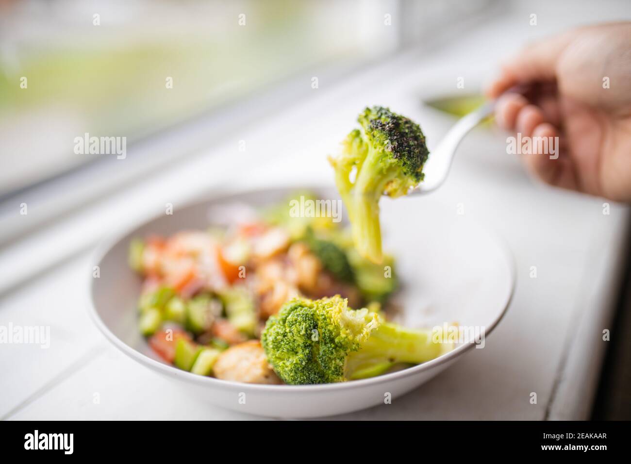 Fourchette de cueillette de brocoli à partir d'un brocoli et salade de poulet ensuite à une fenêtre Banque D'Images