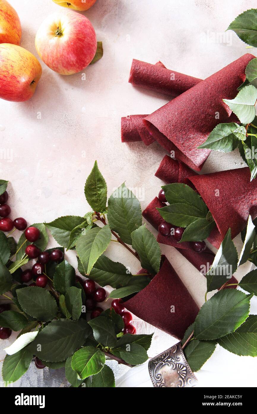 Pastilles de cerise et pommes sur fond clair. Produit naturel sans colorants ni conservateurs. La pastille est enroulée sous forme de cône. Nourriture pour un en-cas sain. Banque D'Images