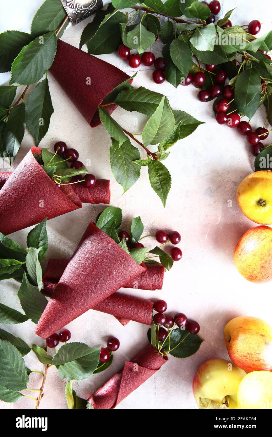 Sucrée à base de cerises et de pommes.pastilles de cerises et pommes sur fond clair. Produit naturel sans colorants ni conservateurs. La pastille est enroulée sous forme de cône. Nourriture pour un en-cas sain. Banque D'Images