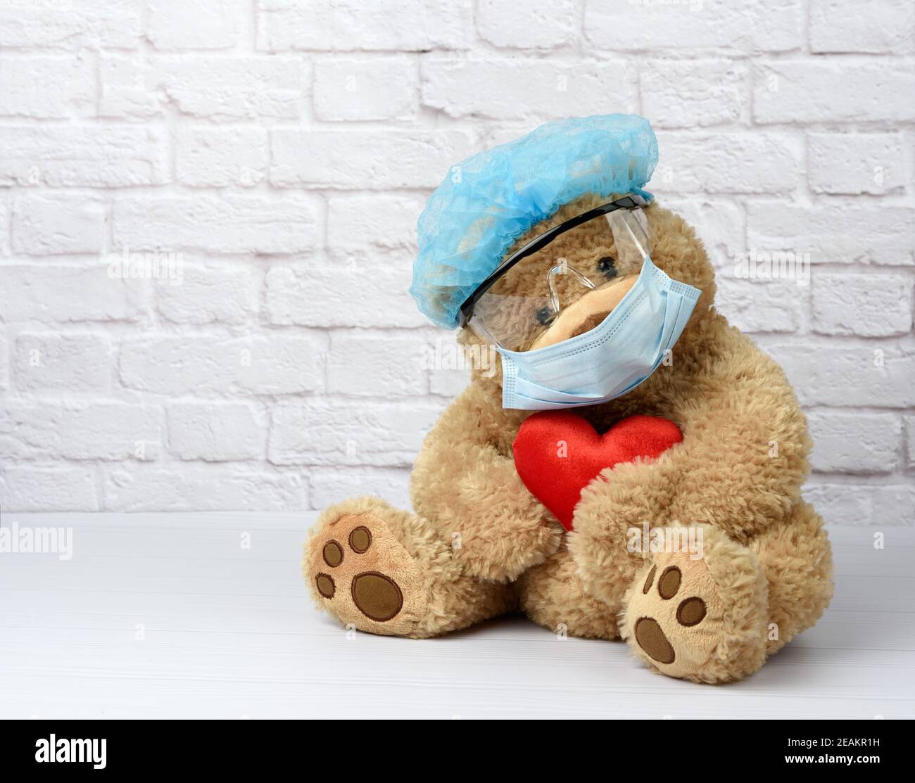 l'ours en peluche brun est assis dans des lunettes de protection en plastique, un masque médical jetable et un capuchon bleu Banque D'Images