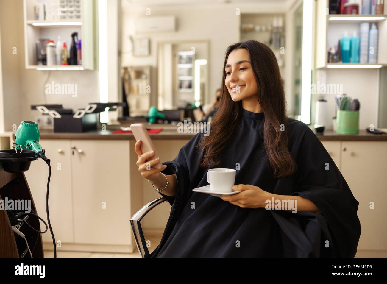 Client féminin avec téléphone et café, salon de coiffure Banque D'Images