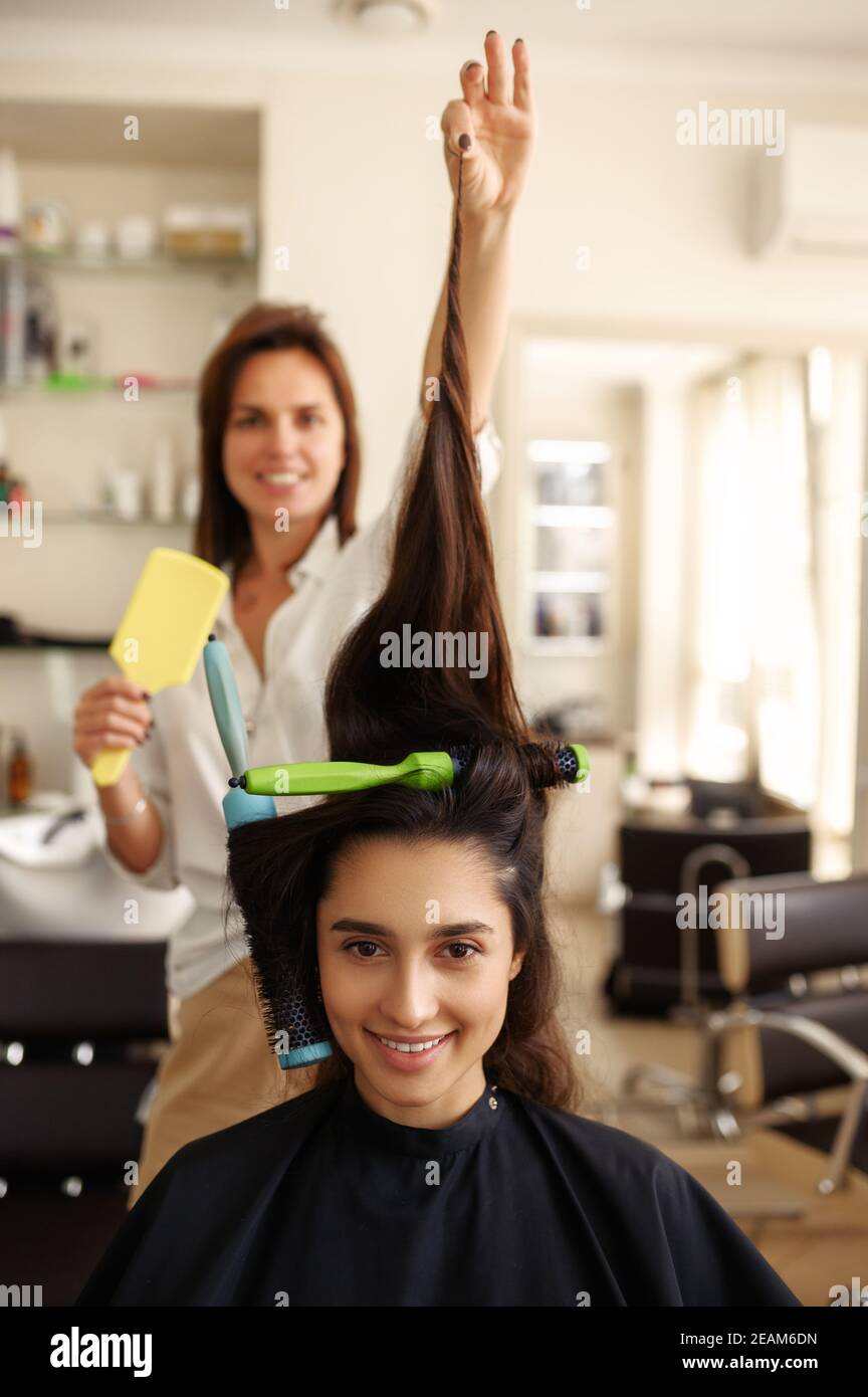 La coiffeuse féminine courbe les cheveux de la femme, salon de coiffure Banque D'Images