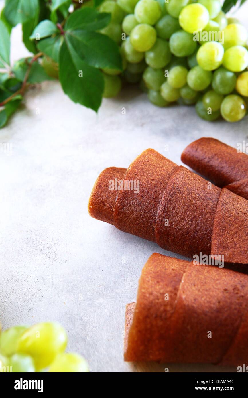 Le guimauve de raisin à lumière naturelle est enroulé dans un tube. Produit naturel sans conservateurs. Nourriture pour végétariens. Photo sur fond clair. Vue de dessus. Banque D'Images