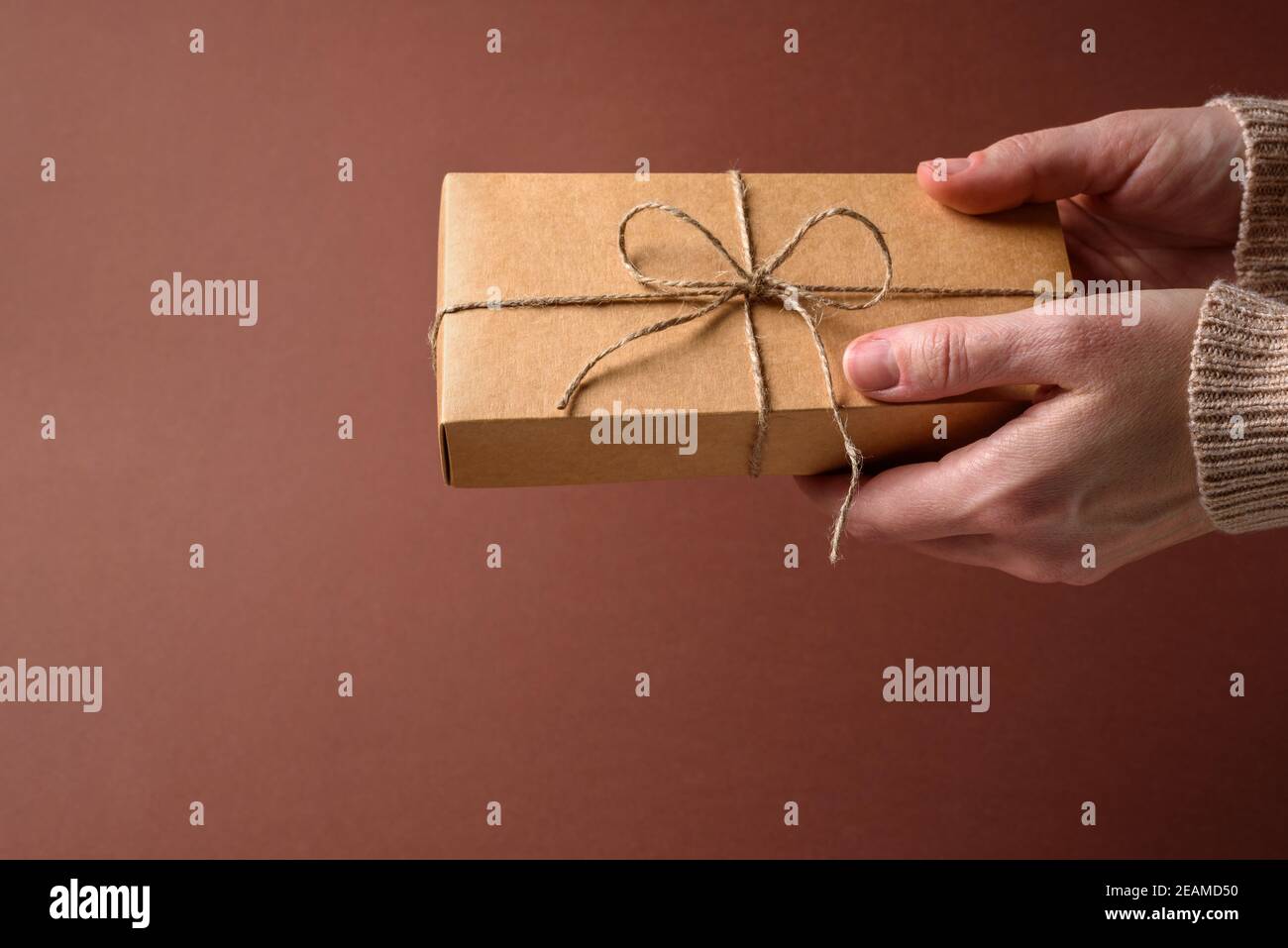 Boîte-cadeau simple en papier avec noeud de ficelle dans les mains de femme sur marron Banque D'Images