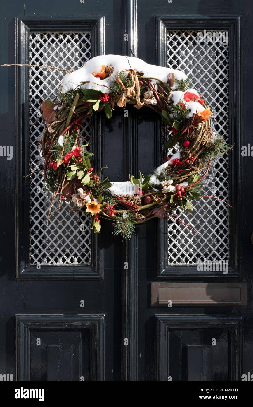 Une couronne de Noël enneigée est suspendue à une porte avant décorée d'une maison à IJlst, Frise, en hiver. Image verticale Banque D'Images