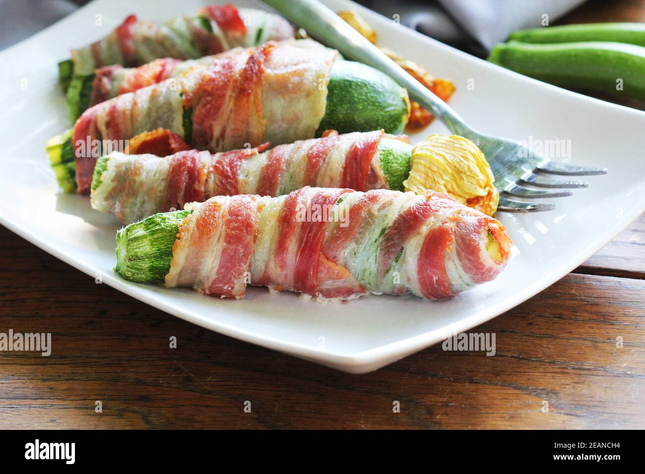 Des courgettes grillées enveloppées dans un bacon sur une plaque blanche Banque D'Images