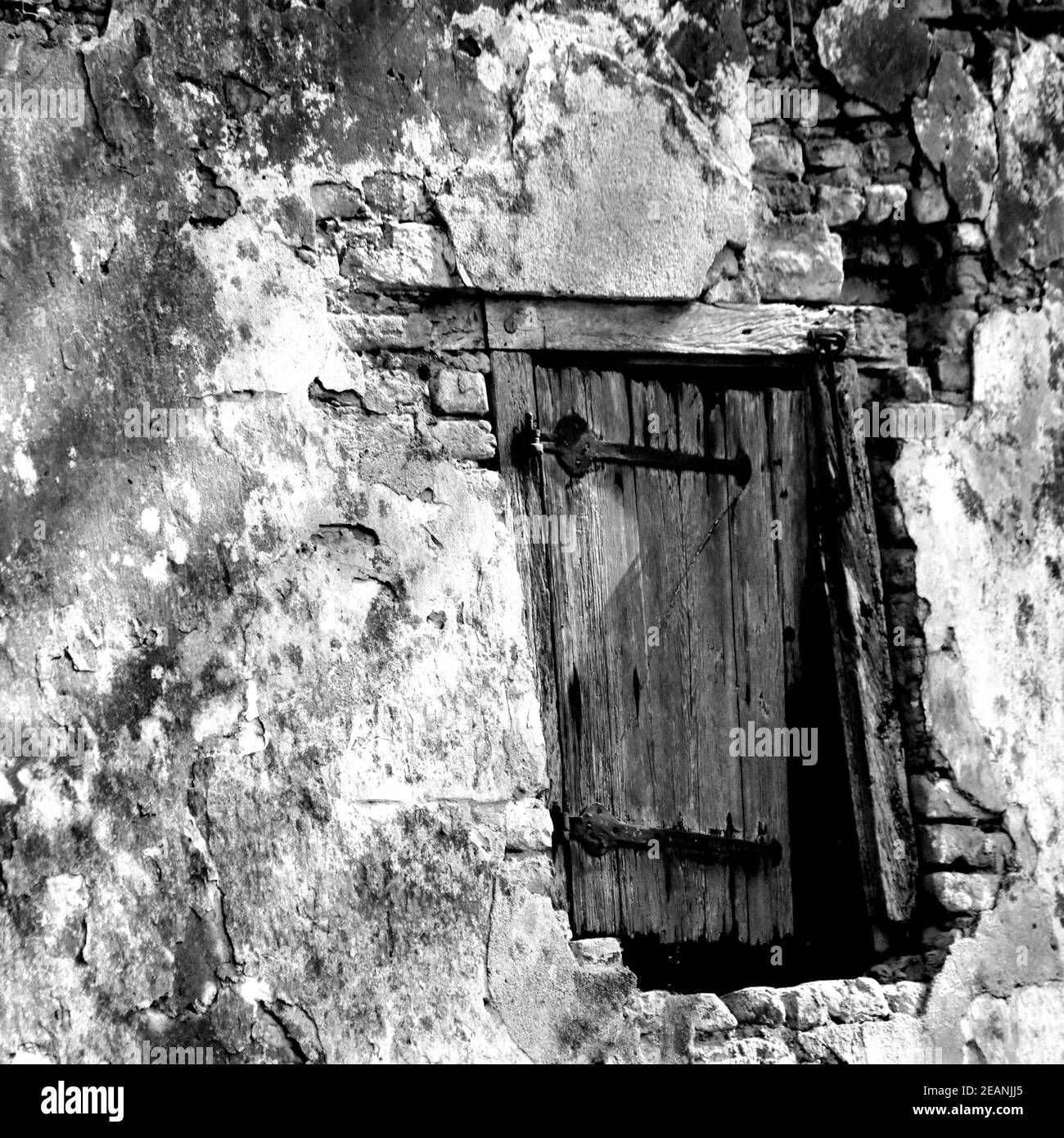 Gros plan d'un mur de maison ancienne avec un petit fenêtre dans une forêt en noir et blanc Banque D'Images