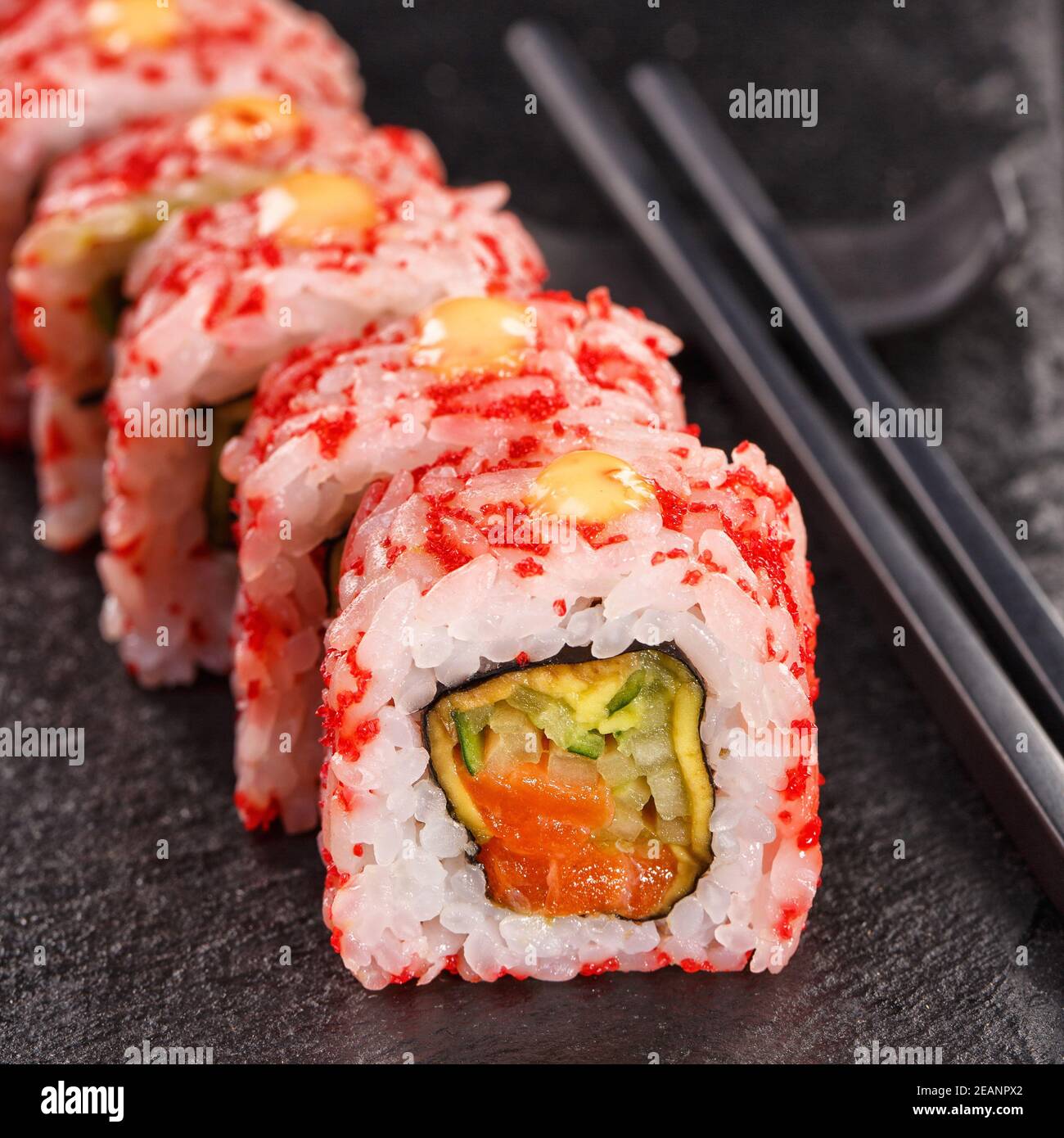 Rouleaux de sushis uramaki recouverts de caviar rouge, remplis de saumon et de concombre. Servi sur un panneau en pierre noire. Banque D'Images