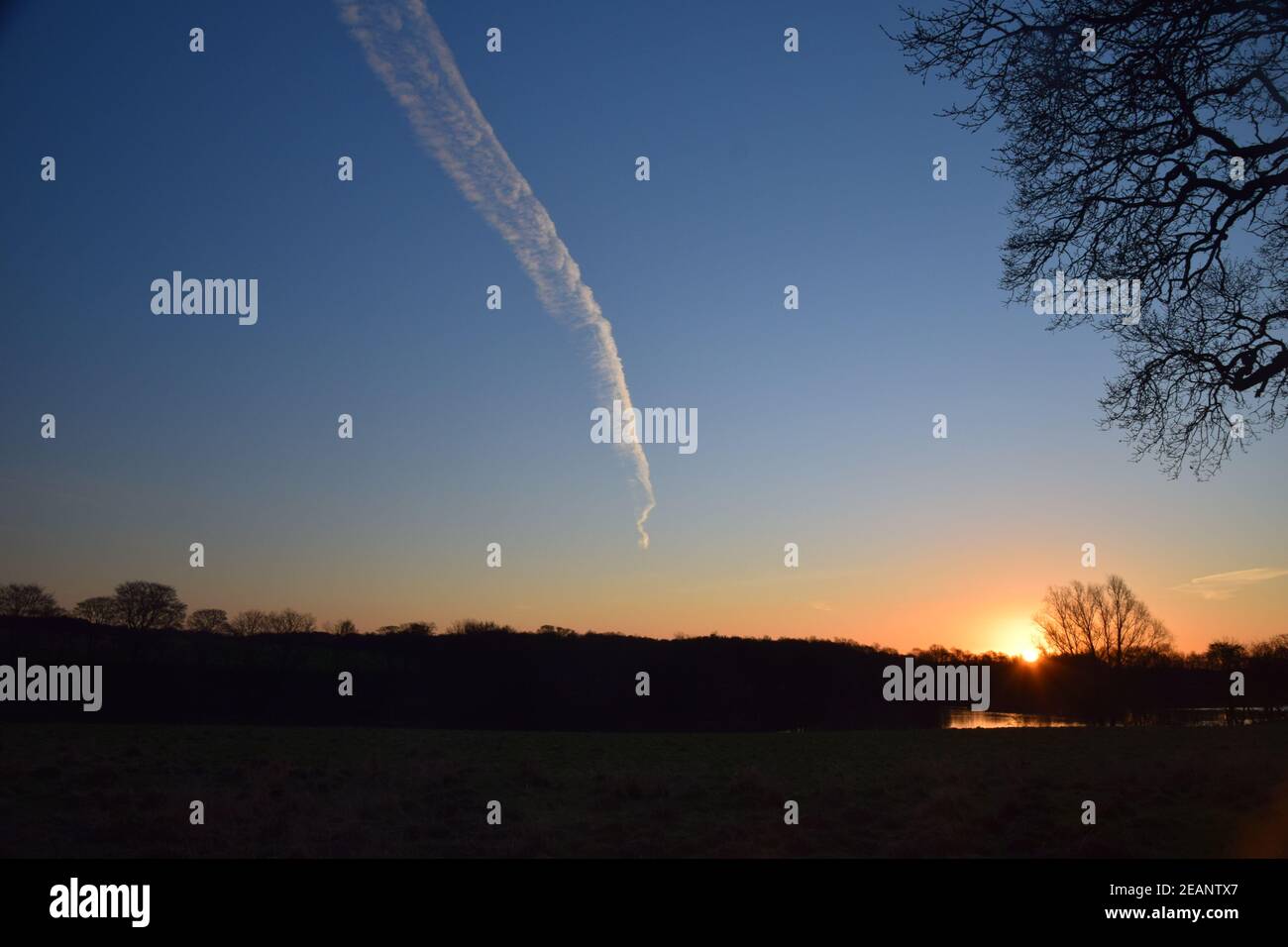 Le soleil levant et un jet stream se rencontrent à l'horizon. Banque D'Images