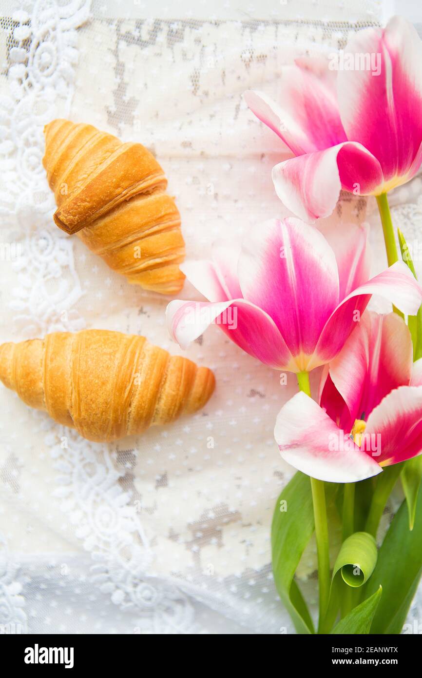 Trois croissants et de tulipes rose vif sur nappe en dentelle, close-up Banque D'Images