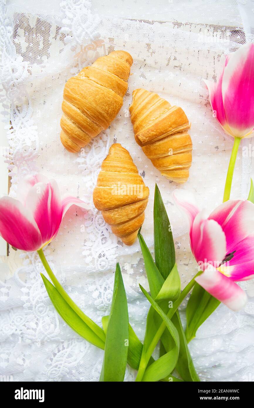 Trois croissants et de tulipes rose vif sur nappe en dentelle Banque D'Images