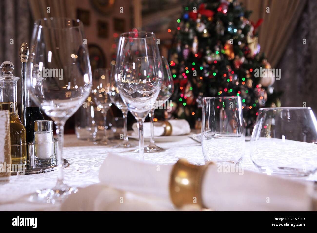 Paramètre de table pour la nouvelle année. L'arbre de Noël est hors foyer. Beaucoup de verres vides sur la table. Photo à l'intérieur. Banque D'Images