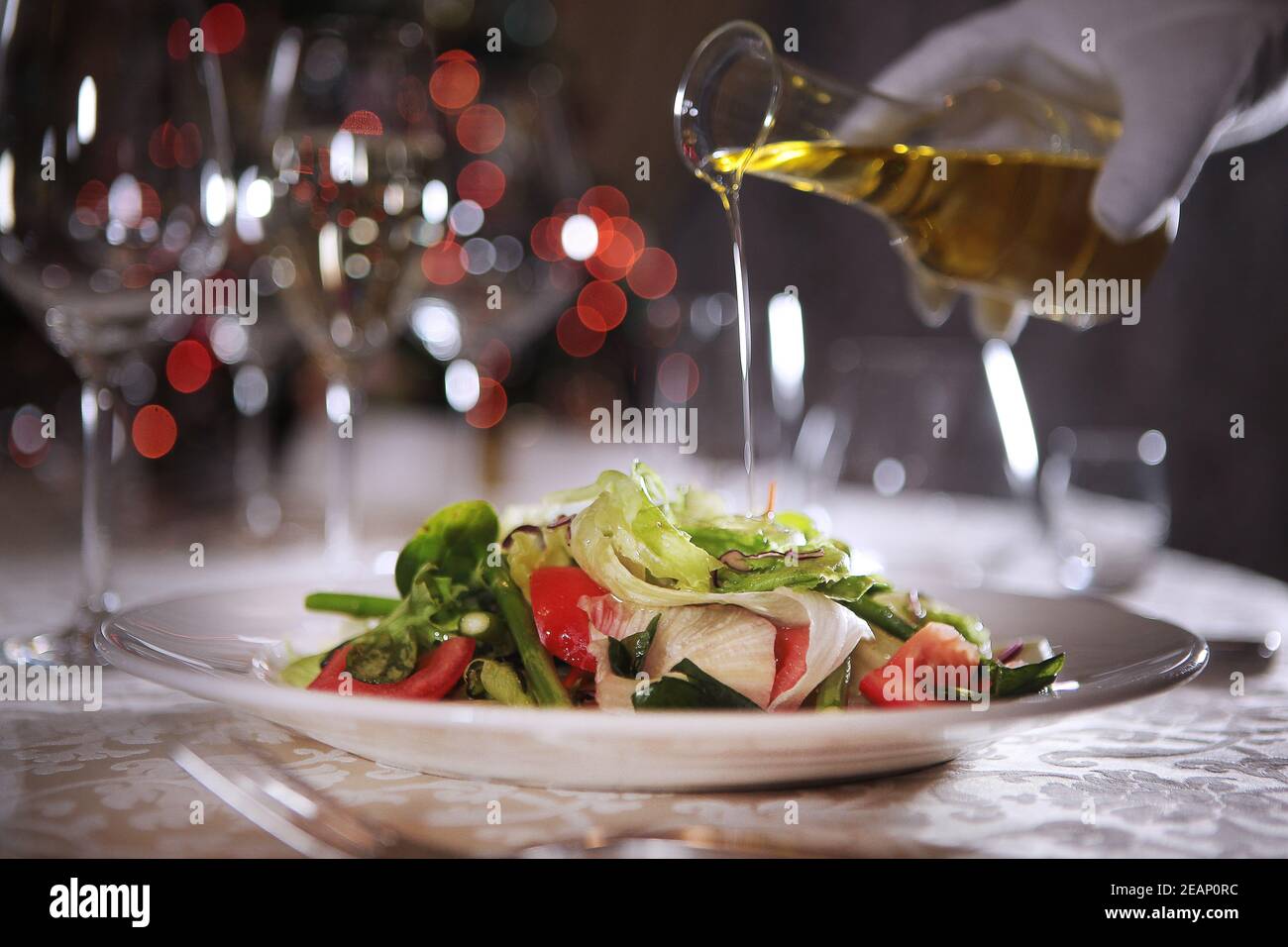 L'huile d'olive est versée sur la salade préparée. Bras hors foyer. Photos sans visage. Banque D'Images
