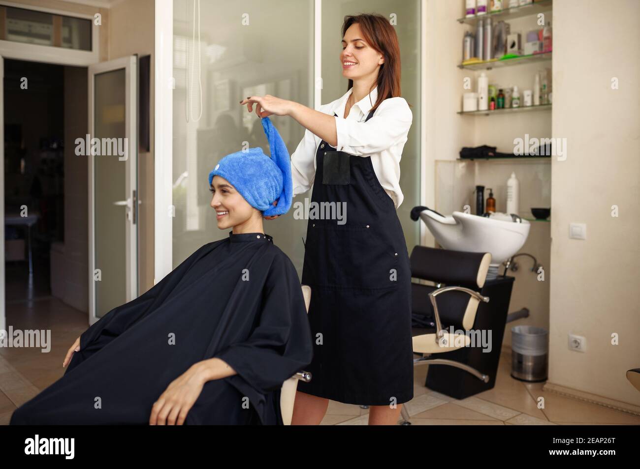 Le coiffeur met une serviette sur les cheveux de la femme, vue de face Banque D'Images