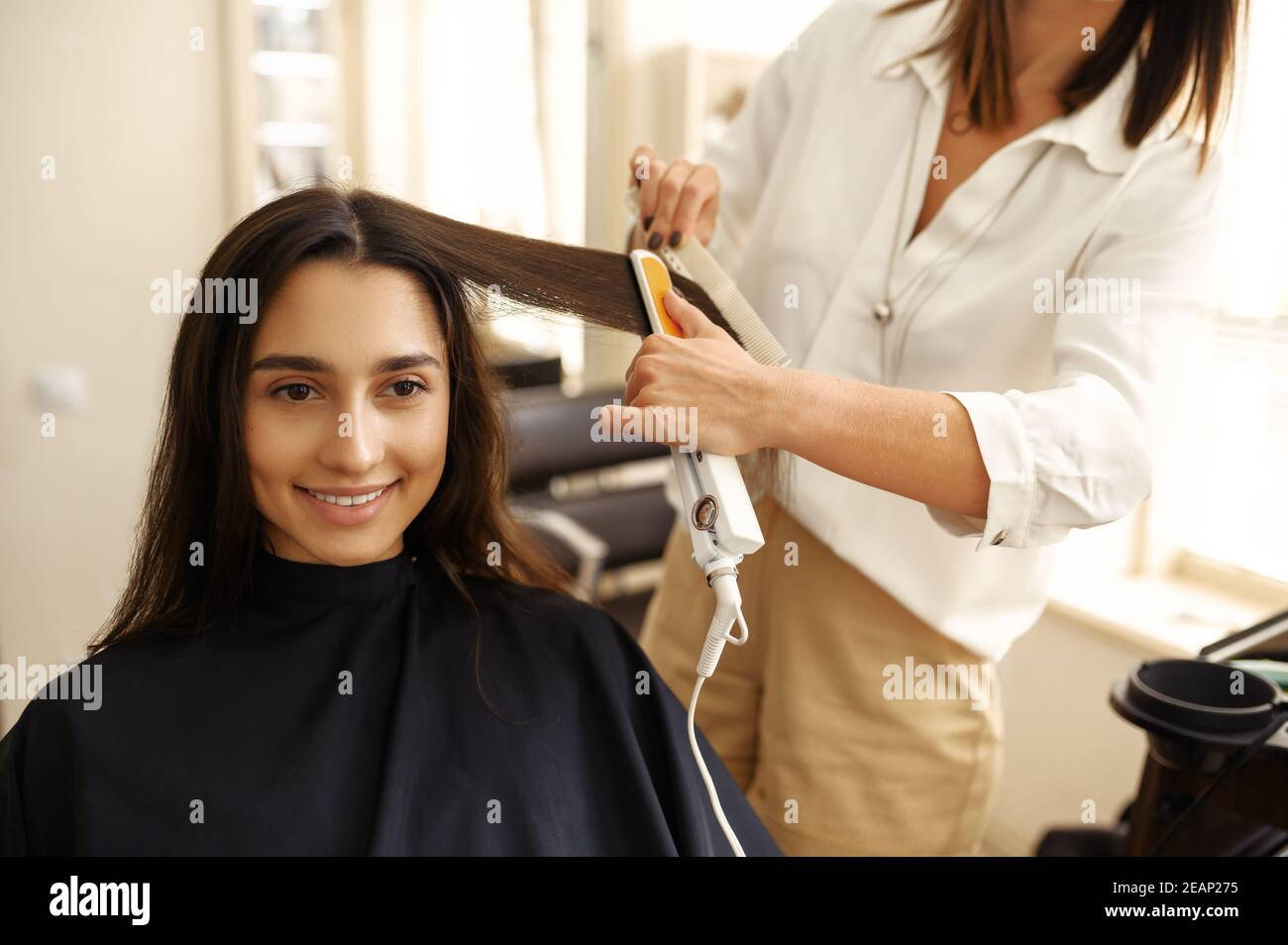 Coiffeur redresse les cheveux de la femme, salon de coiffure Banque D'Images
