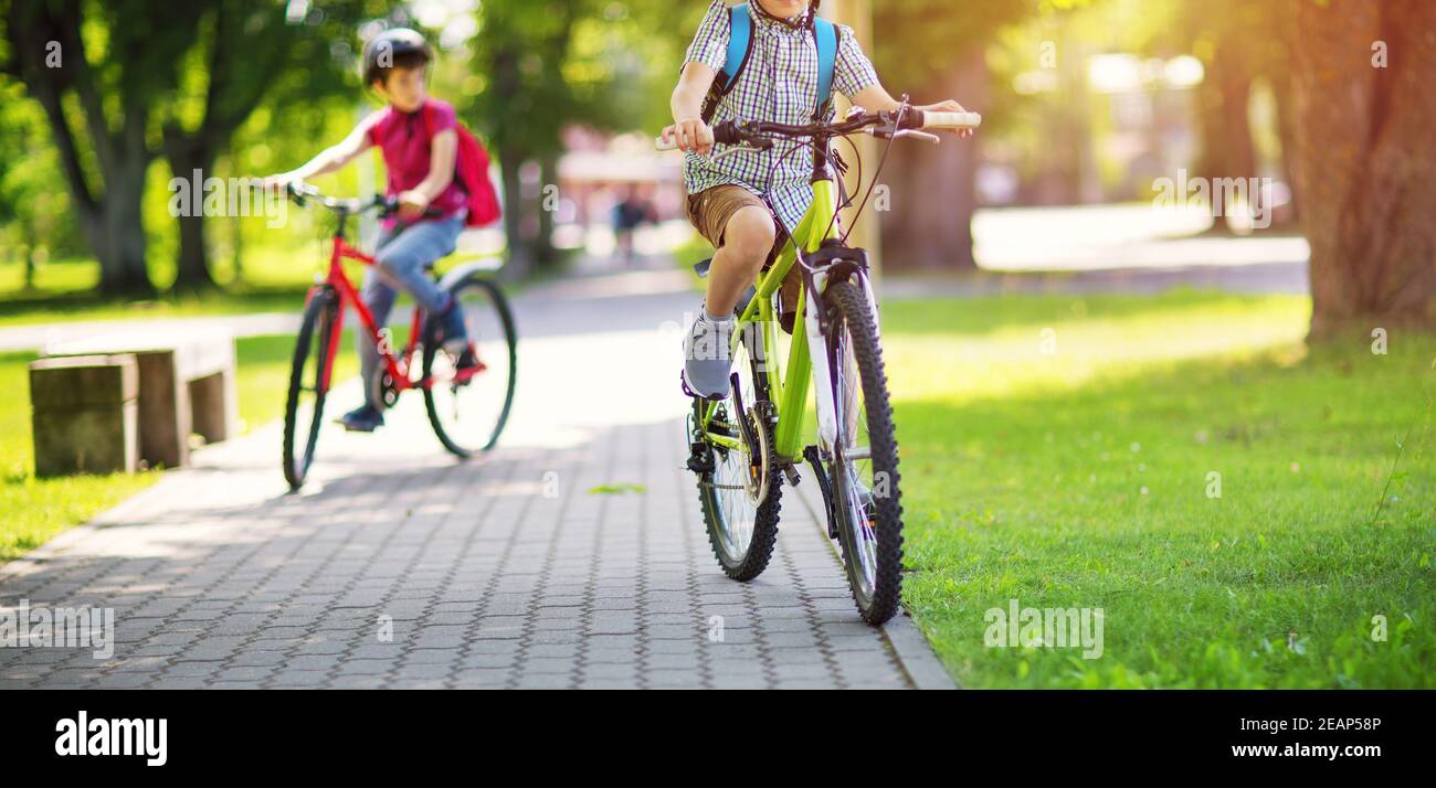 Les enfants avec des sacs à dos équitation sur des vélos dans le parc près de l'école Banque D'Images