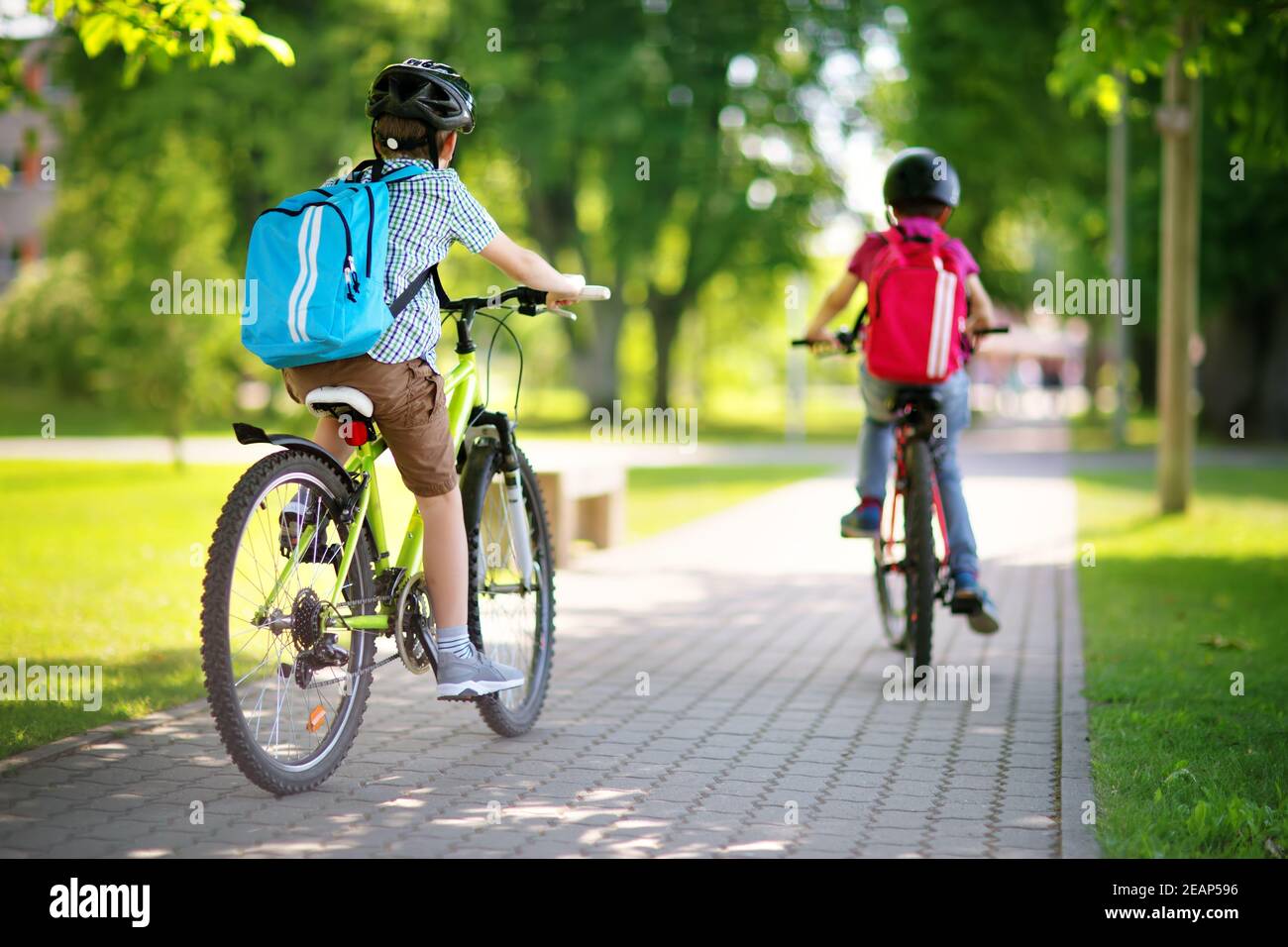 Les enfants avec des sacs à dos équitation sur des vélos dans le parc près de l'école Banque D'Images
