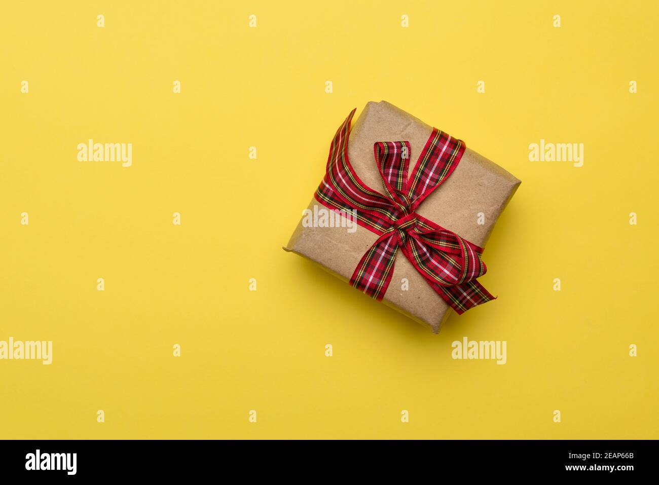 boîte carrée avec un cadeau enveloppé dans du papier brun et attaché avec un ruban rouge de soie Banque D'Images