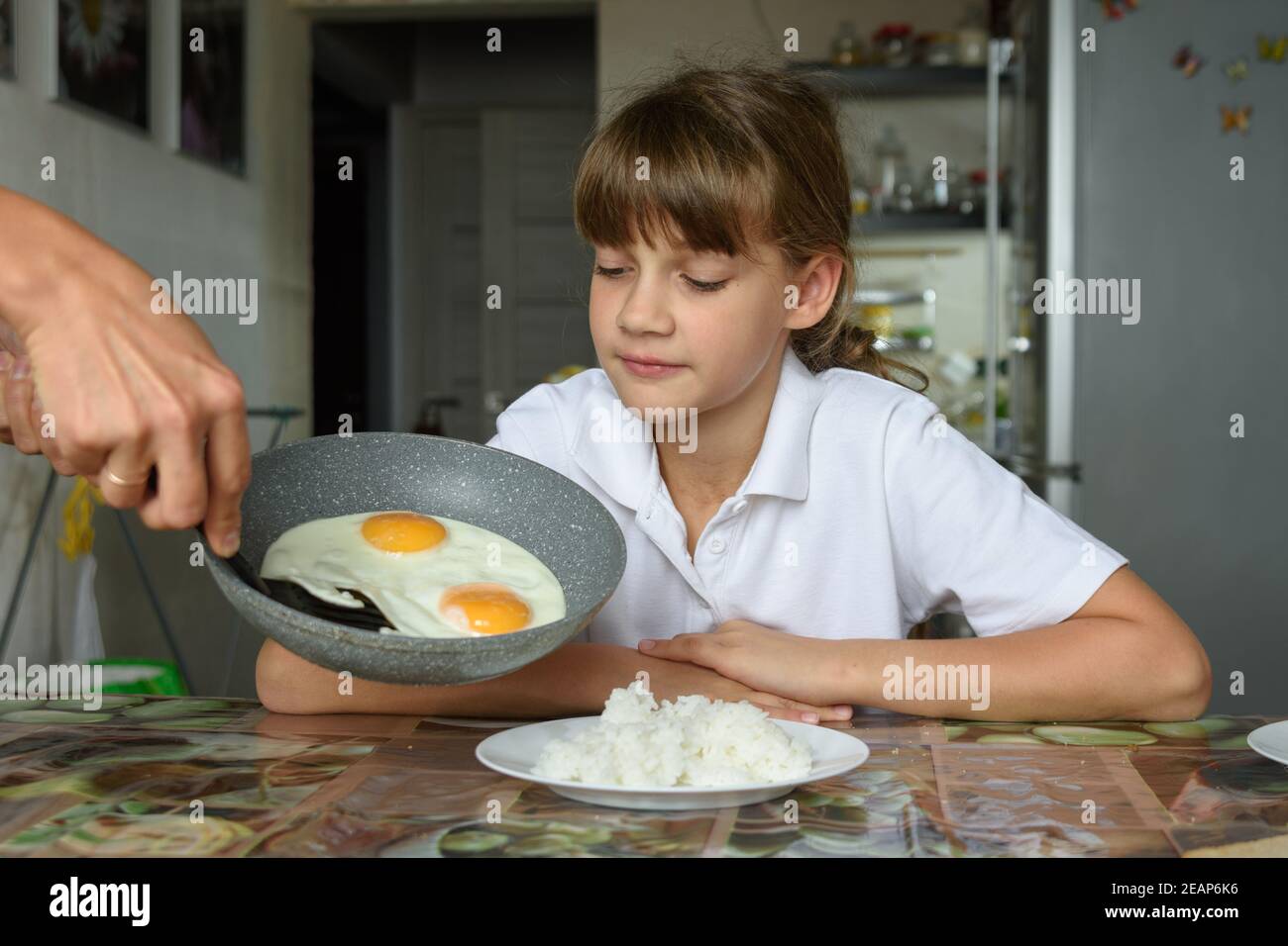 Maman cuit des œufs brouillés pour le déjeuner et les met de la casserole sur la plaque de la fille Banque D'Images