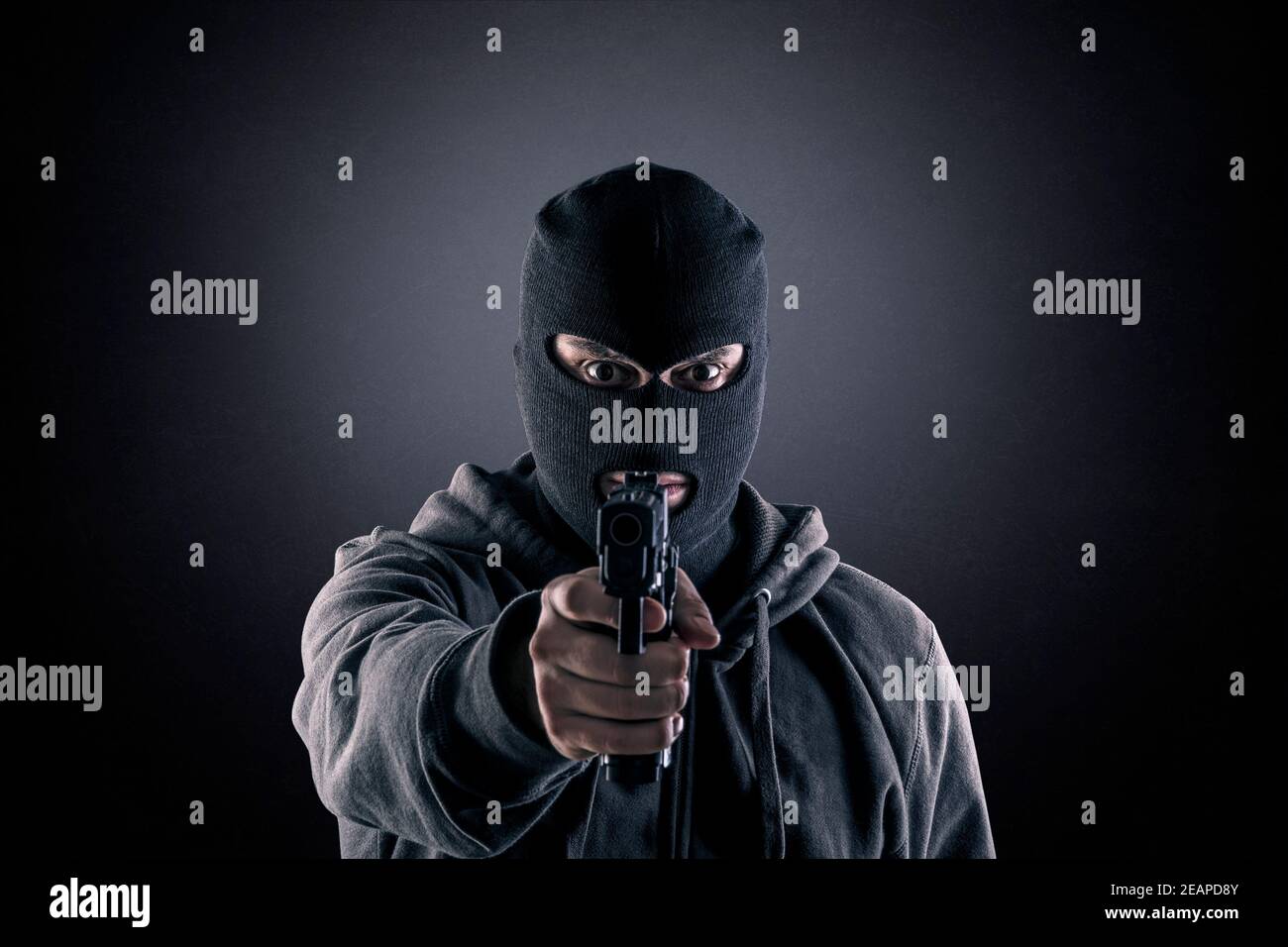 Criminel portant de la balaclava noire et un sweat à capuche avec une arme à feu dedans le noir Banque D'Images