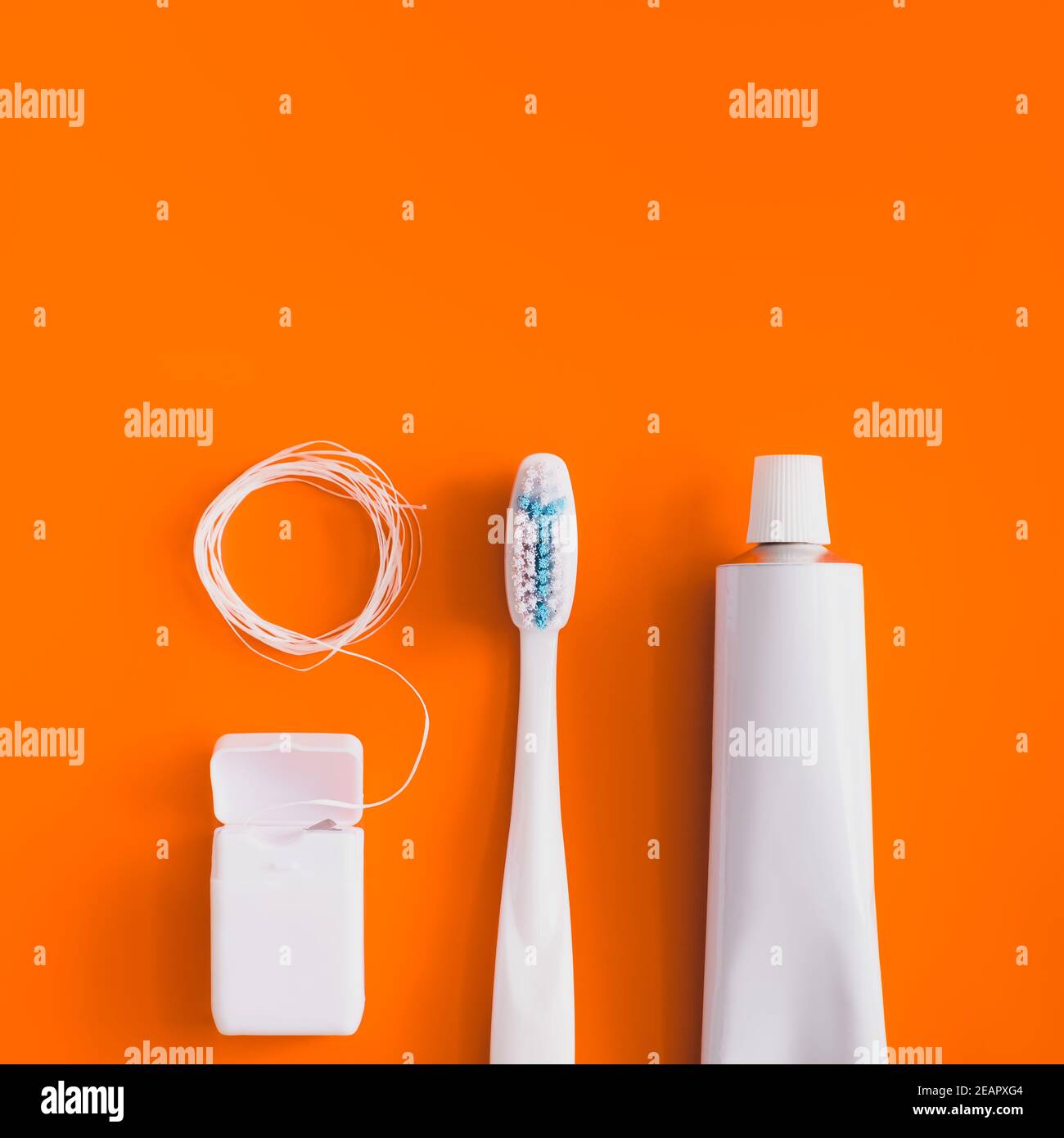 Objets d'hygiène dentaire : brosse à dents, dentifrice et soie dentaire. Accessoires génériques blancs pour maintenir la santé des dents sur fond orange vif Banque D'Images