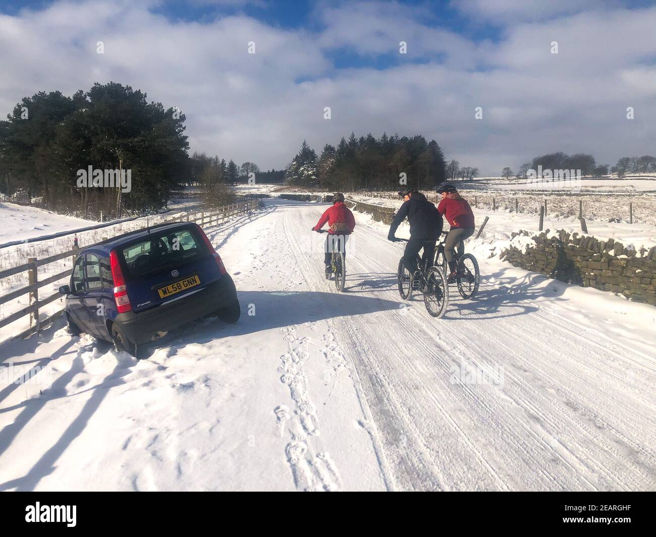 Trois cyclistes passent devant une voiture qui s'est écrasée dans la neige à Sheffield, dans le South Yorkshire, en Angleterre Banque D'Images